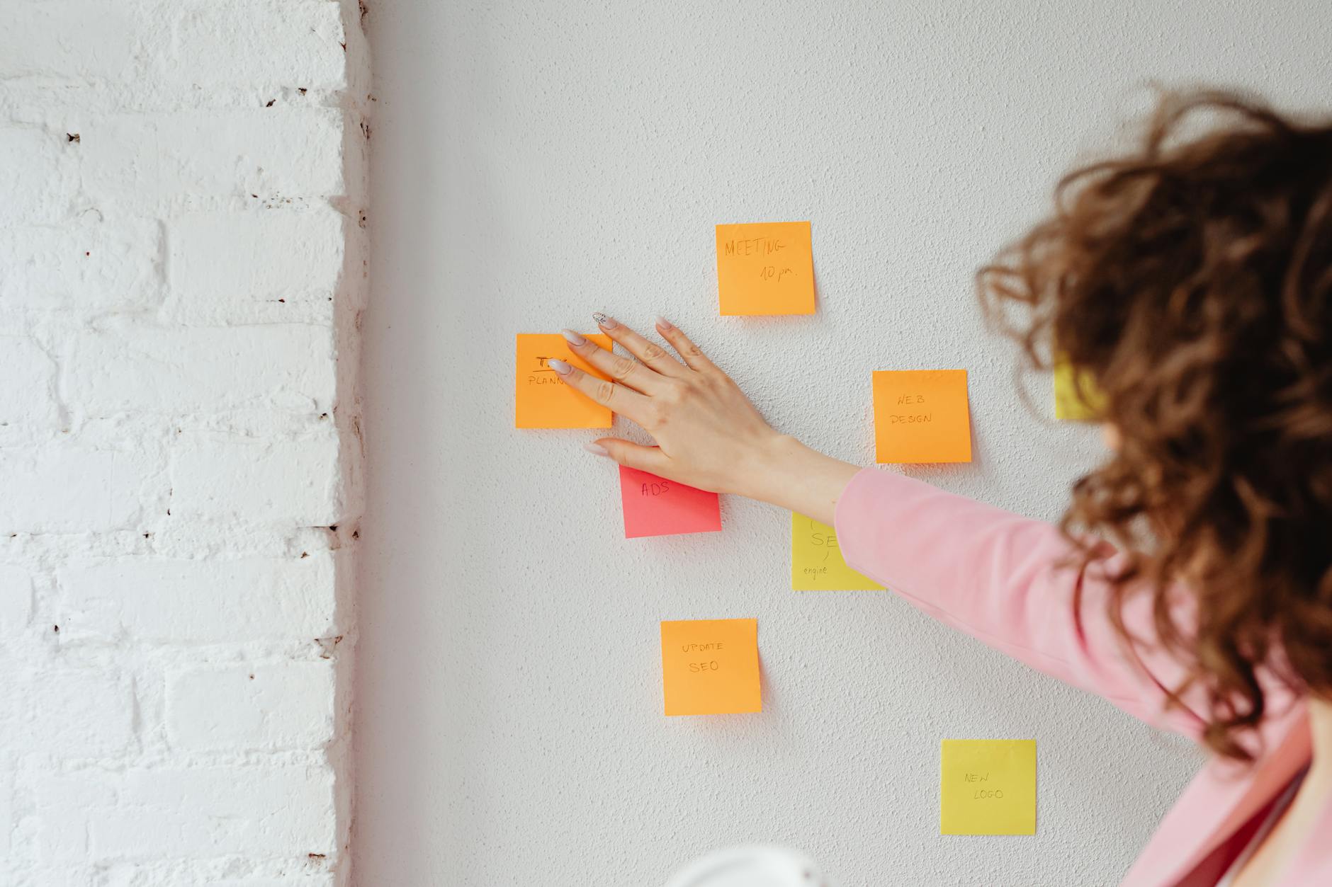 A woman planning ideas with colourful sticky notes on a wall, mapping a positioning hypothesis.