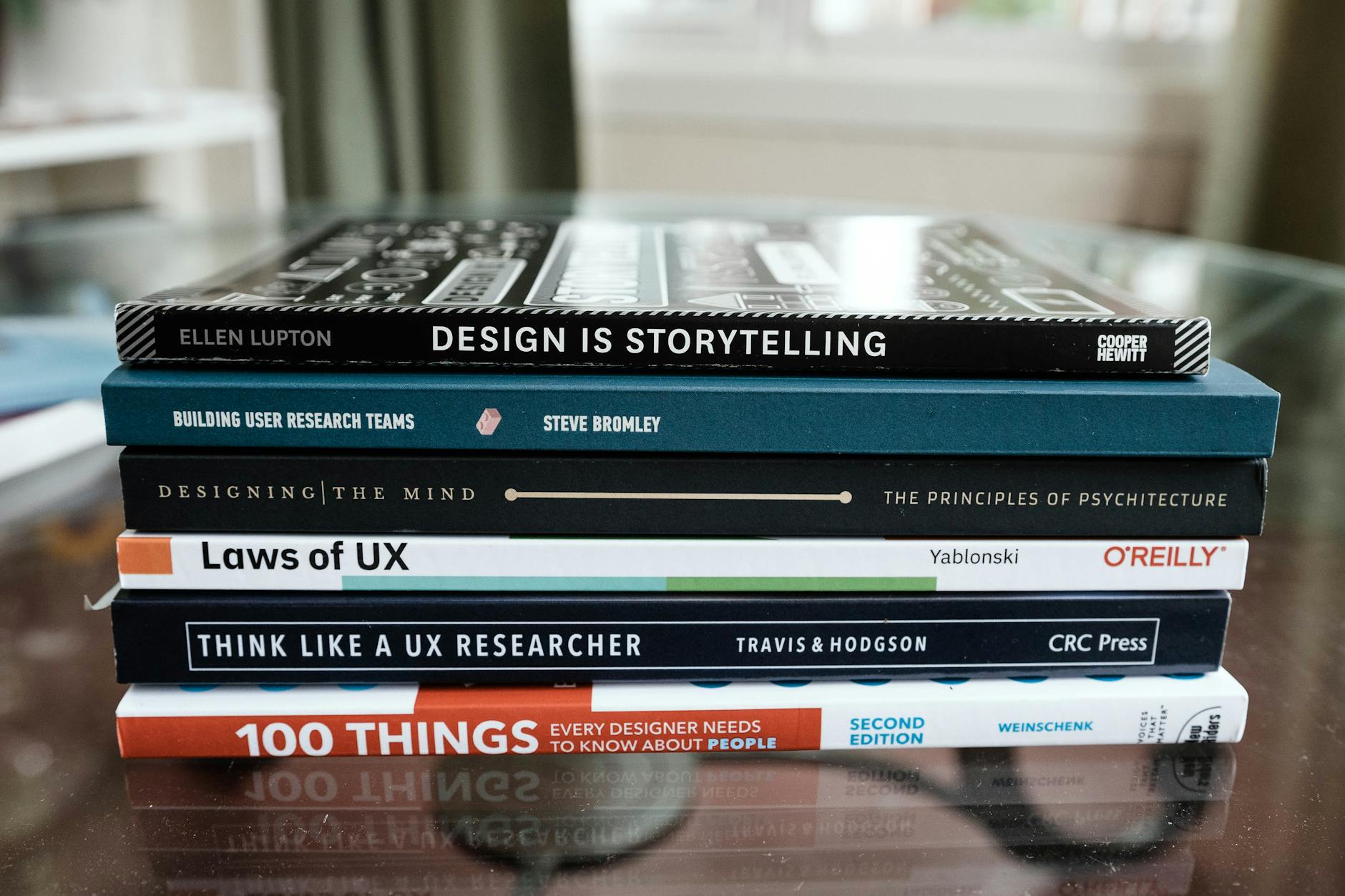 Brand guidelines — design reference books A close-up of books focused on design and UX research stacked on a glass table.